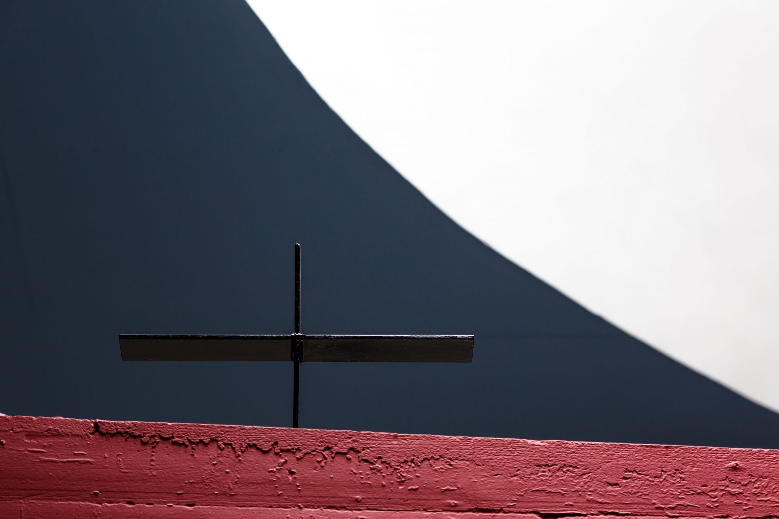 Détail de l'église du Couvent de la Tourette. Une croix en métal sur un mur de béton brut peint en rouge et le puit de lumière blanc