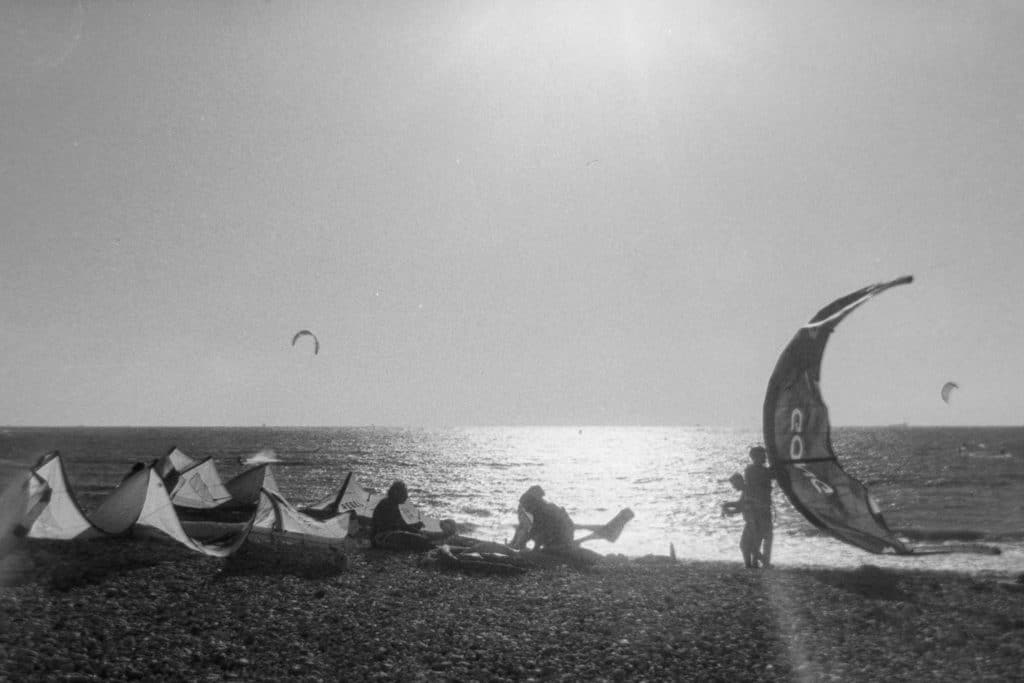 Coucher de soleil sur la plage du Havre avec les voiles posée sur les galets et des silouhettes de surfeur en contre jour