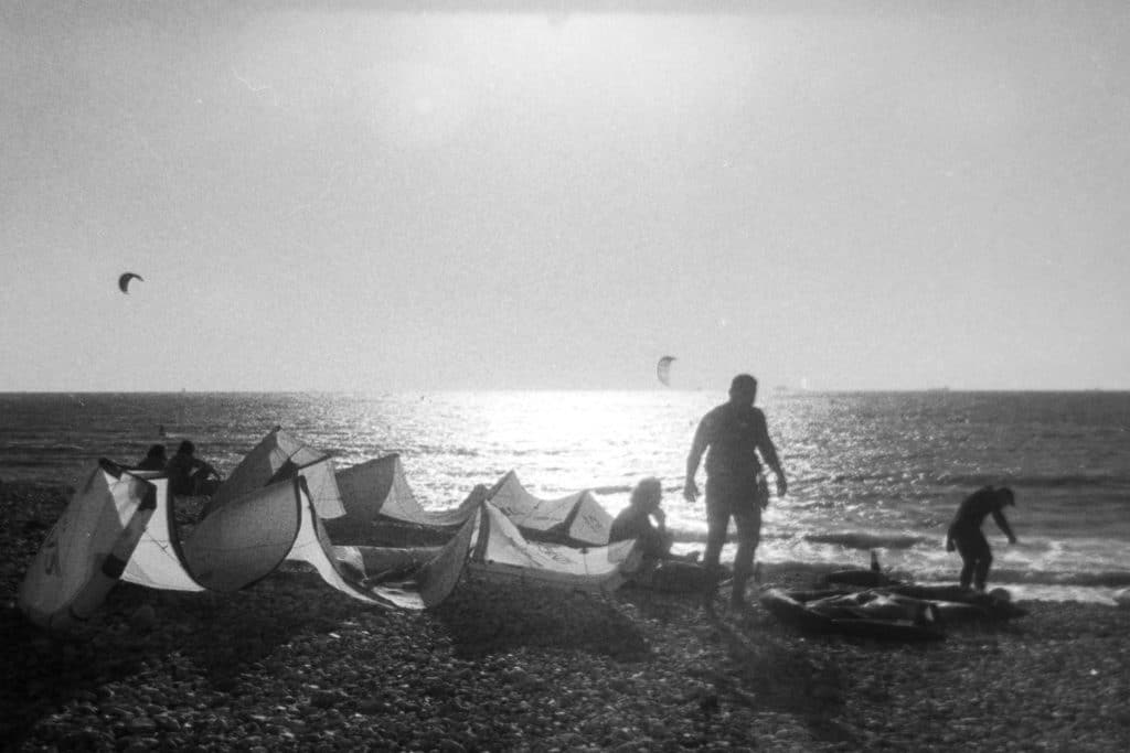 Coucher de soleil sur la plage du Havre avec les voiles posée sur les galets et des silouhettes de surfeur en contre jour